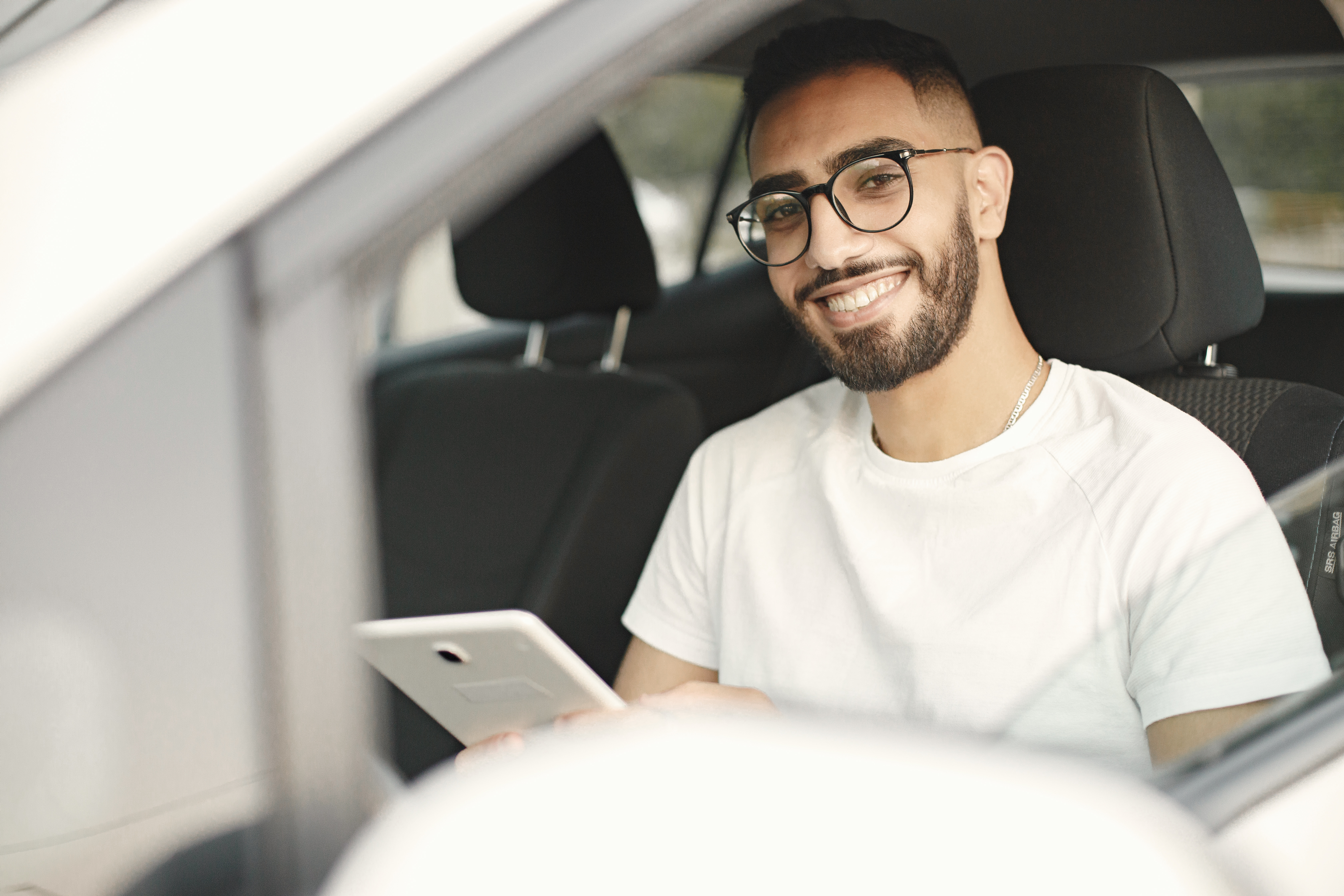 Homem manuseando um tablet, dentro de um veículo. Foto: Freepik
